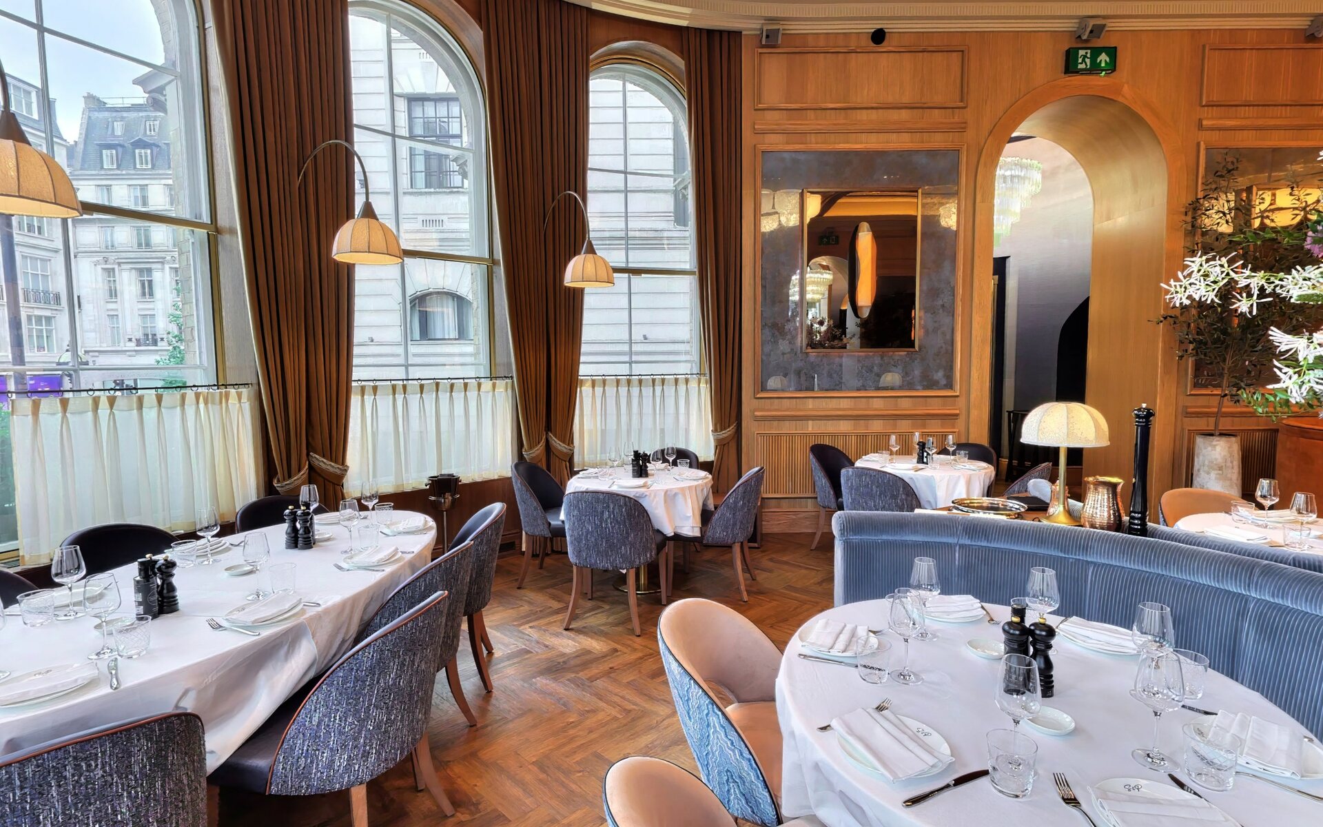 Dining tables set beneath the tall arched windows with warm London light